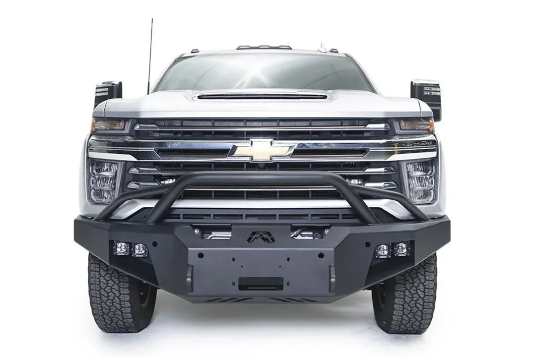Fab Fours Premium Winch front bumper with pre-runner guard on a white Chevrolet Silverado 2500HD, straight-on front view, showing the pre-runner guard, the center winch plate, Fab Fours logo and cube light pods