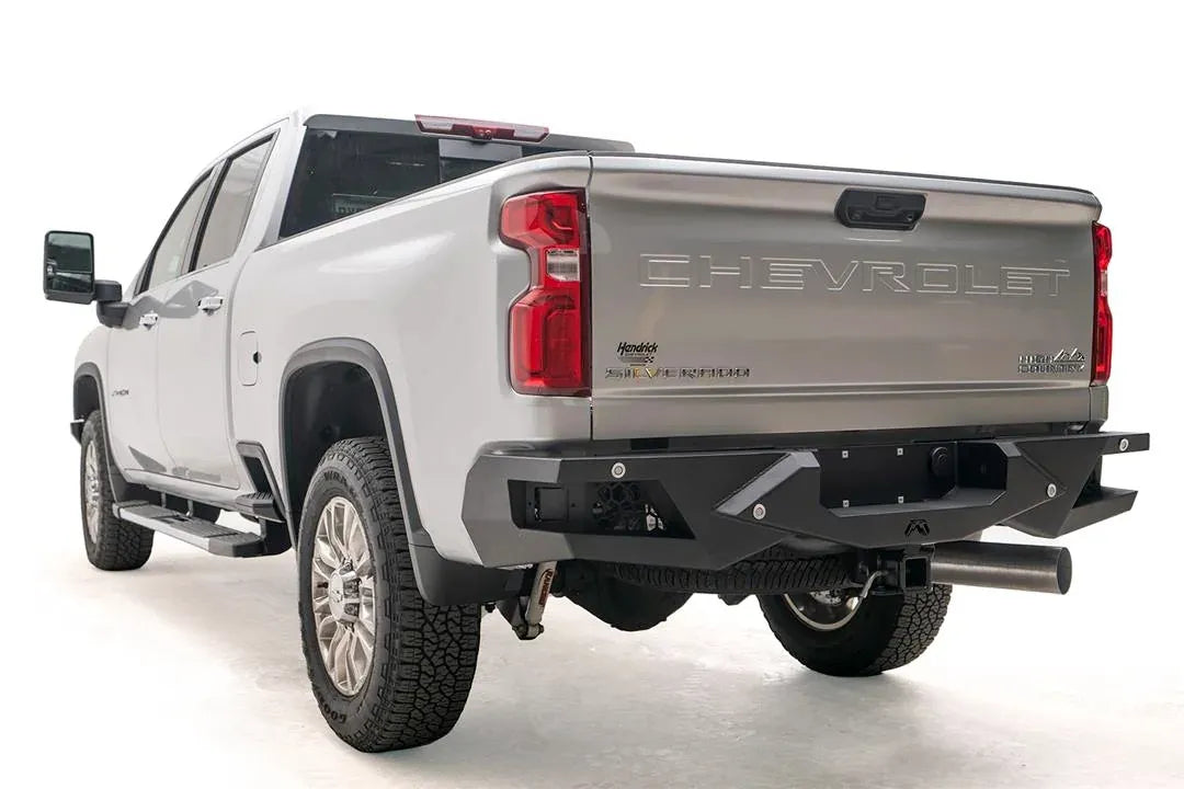 Fab Fours Vengeance rear bumper on a silver Chevrolet Silverado 2500HD, rear driver-side three-quarter view, showing the honeycomb light pods, angular end caps and center hitch opening