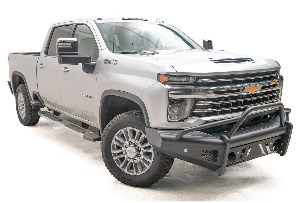 Fab Fours Black Steel Elite front bumper with pre-runner guard on a silver Chevrolet Silverado 2500HD, front passenger-side three-quarter view, showing the pre-runner guard, slotted skid plate and mesh light openings
