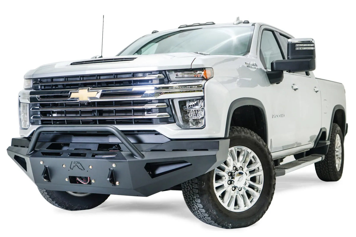 Fab Fours Red Steel front bumper with pre-runner guard on a white Chevrolet Silverado 2500HD, front driver-side three-quarter view, showing the pre-runner guard, angular bumper face, Fab Fours logo and winch hook