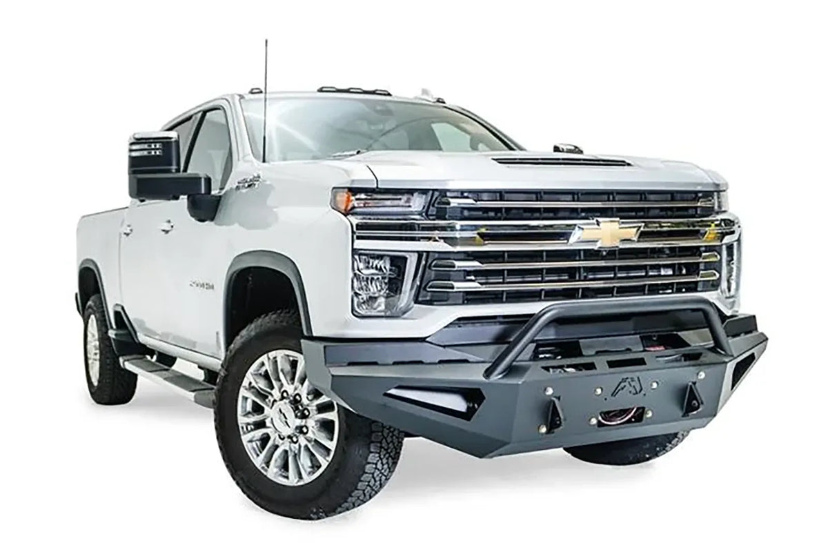 Fab Fours Red Steel front bumper with pre-runner guard on a white Chevrolet Silverado 2500HD, front passenger-side three-quarter view, showing the pre-runner guard, angular bumper face, Fab Fours logo and winch hook