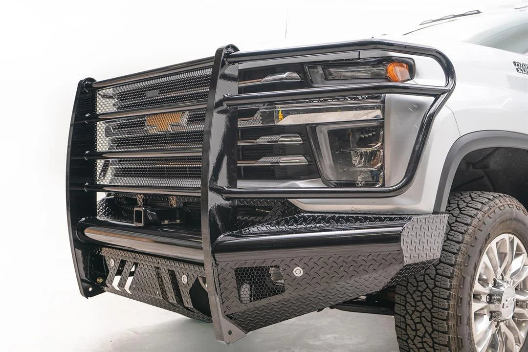 Fab Fours Black Steel front bumper with full guard on a white Chevrolet Silverado 2500HD, close-up of the front corner, showing the mesh-filled guard, diamond-plate end cap and lower skid slots