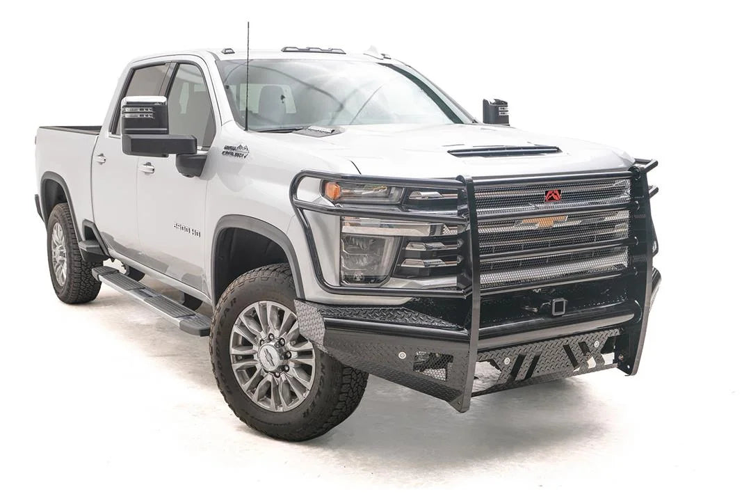 Fab Fours Black Steel front bumper with full guard on a white Chevrolet Silverado 2500HD, front passenger-side three-quarter view, showing the full grille guard, diamond-plate wings and integrated light mounts