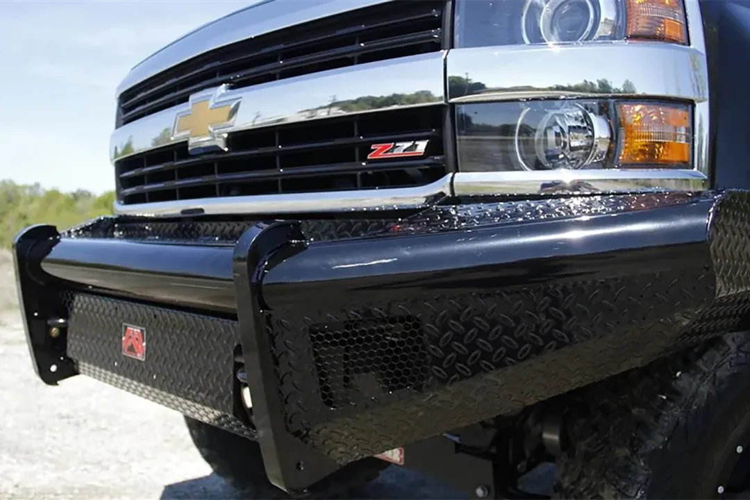 Fab Fours Black Steel front bumper on a black Chevrolet Silverado, outdoor close-up of the front corner, showing the diamond-plate face, black steel end wing and red Fab Fours logo plate