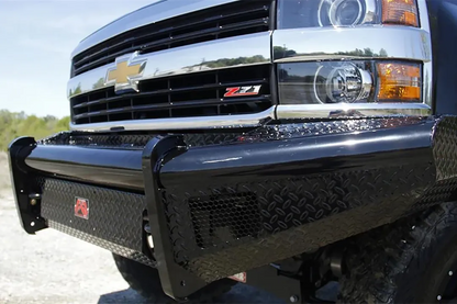 Fab Fours Black Steel front bumper on a black Chevrolet Silverado, outdoor close-up of the front corner, showing the diamond-plate face, black steel end wing and red Fab Fours logo plate