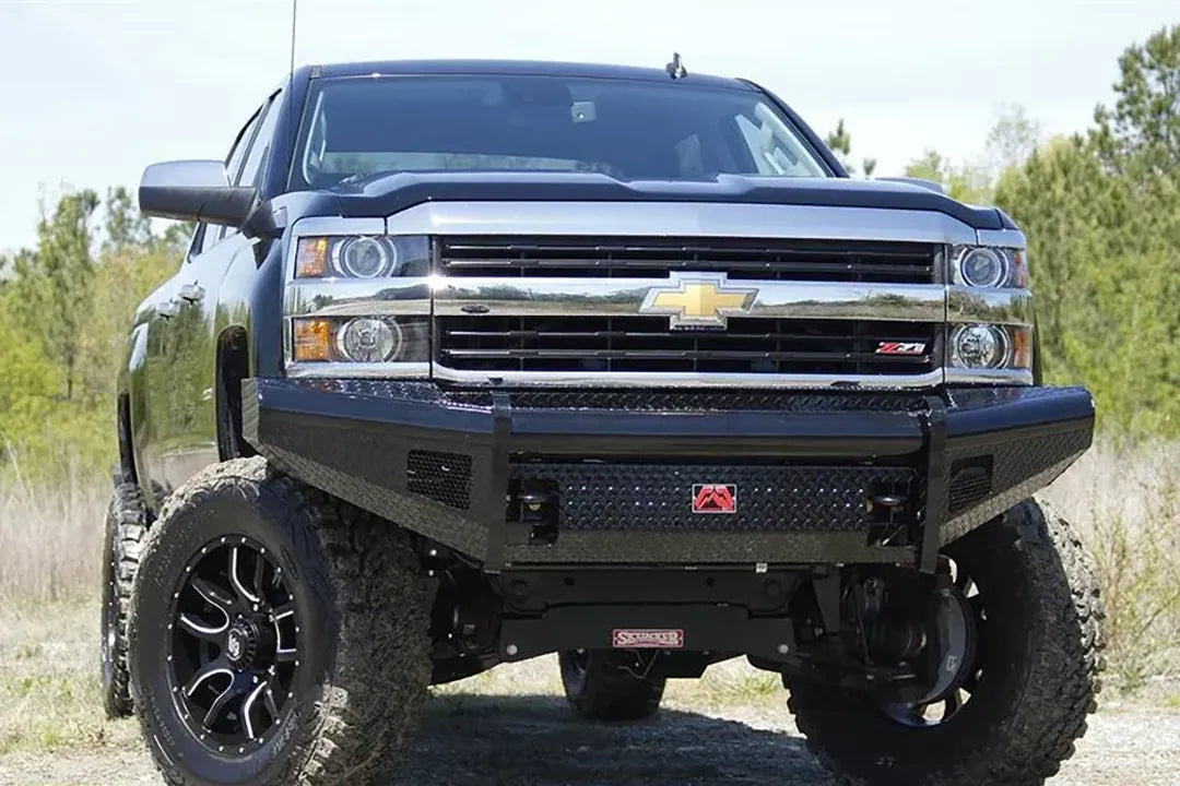 Fab Fours Black Steel front bumper on a black lifted Chevrolet Silverado, outdoor straight-on front view, showing the no-guard design, diamond-plate center panel and red Fab Fours logo plate