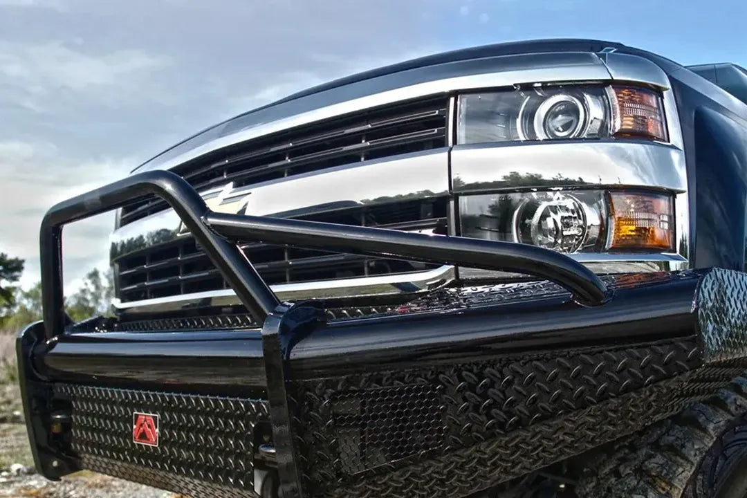 Fab Fours Black Steel front bumper with pre-runner guard on a black Chevrolet Silverado, outdoor close-up of the front corner, showing the tubular pre-runner bar, diamond-plate panels and red Fab Fours logo plate
