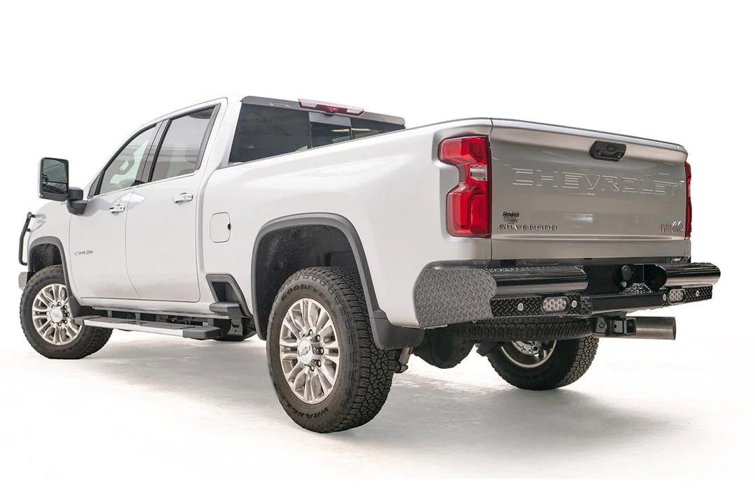 Fab Fours Black Steel rear bumper on a white Chevrolet Silverado 2500HD, rear driver-side three-quarter view, showing the diamond-plate end cap, integrated rear lights and wraparound corner