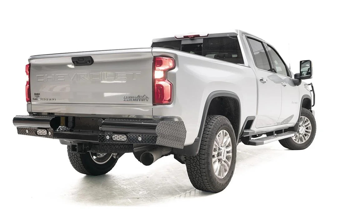 Fab Fours Black Steel rear bumper on a white Chevrolet Silverado 2500HD, rear passenger-side three-quarter view, showing the diamond-plate end caps, flush-mount rear lights and center receiver area