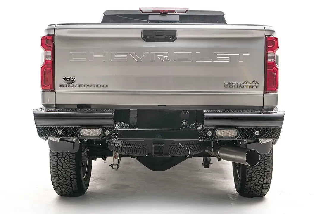 Fab Fours Black Steel rear bumper on a white Chevrolet Silverado 2500HD, straight-on rear view, showing the full-width diamond-plate bumper, recessed lights and center hitch receiver