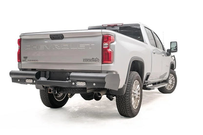 Fab Fours Black Steel Elite rear bumper on a white Chevrolet Silverado 2500HD, rear passenger-side three-quarter view, showing the smooth black steel face, integrated rear lights and wraparound corners