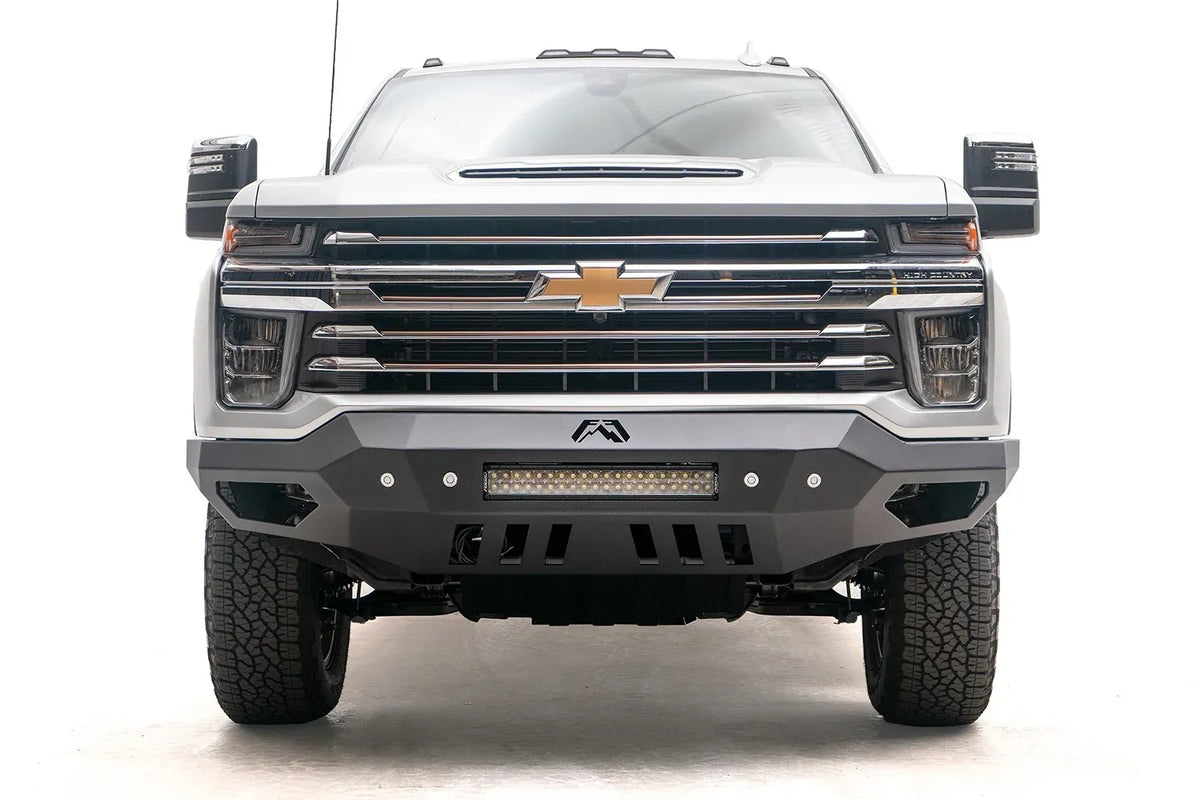 Fab Fours Vengeance front bumper on a white Chevrolet Silverado 2500HD, straight-on front view, showing the full-width bumper face, center light bar and slotted skid plate