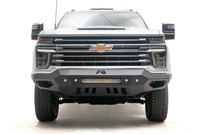 Fab Fours Vengeance front bumper on a white Chevrolet Silverado 2500HD, straight-on front view, showing the full-width bumper face, center light bar and slotted skid plate