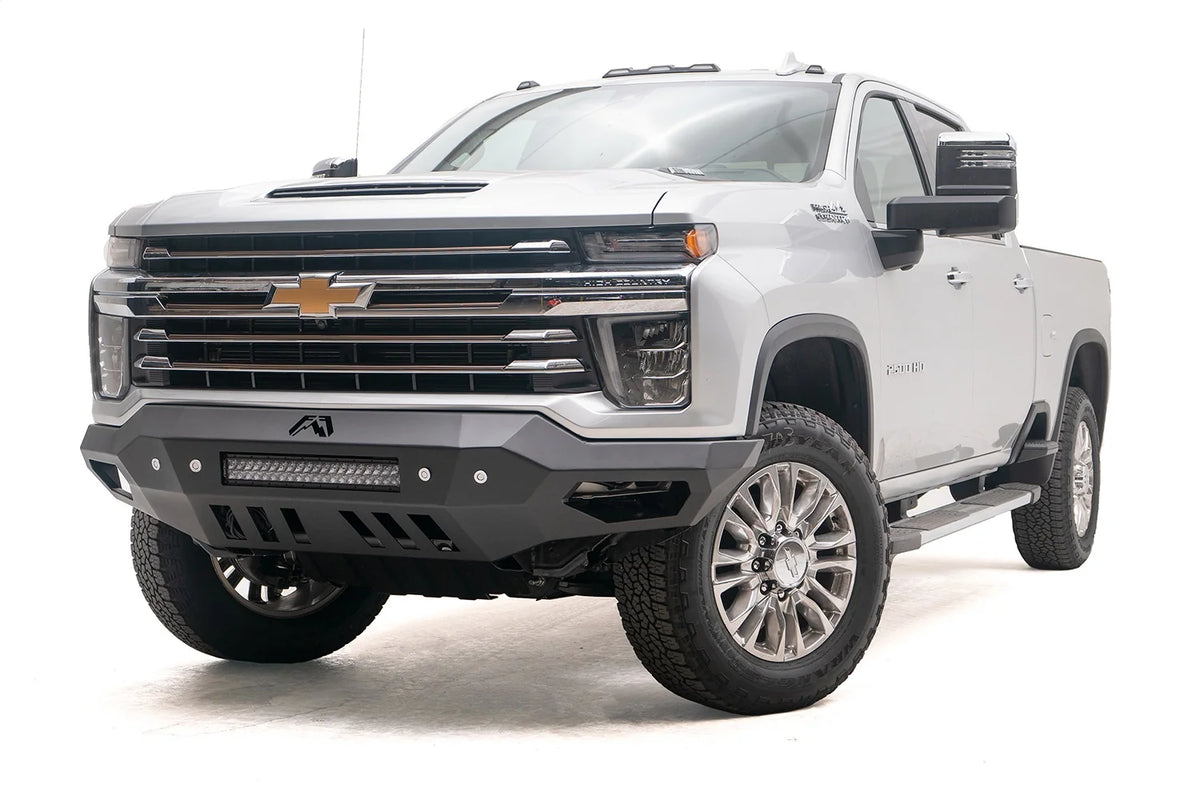 Fab Fours Vengeance front bumper on a white Chevrolet Silverado 2500HD, front driver-side three-quarter view, showing the no-guard design, integrated light bar and angular end wings
