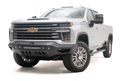 Fab Fours Vengeance front bumper on a white Chevrolet Silverado 2500HD, front driver-side three-quarter view, showing the no-guard design, integrated light bar and angular end wings