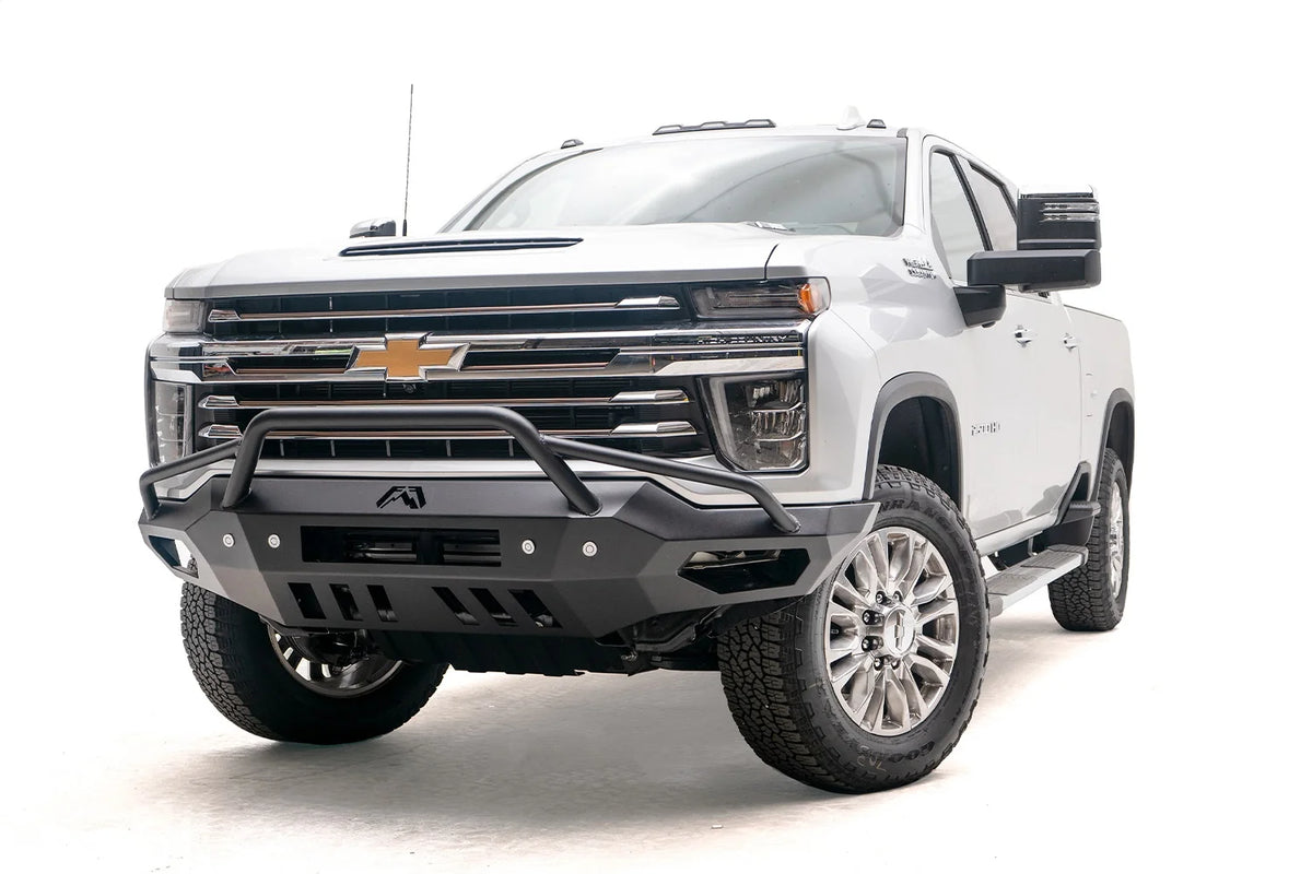 Fab Fours Vengeance front bumper with pre-runner guard on a white Chevrolet Silverado 2500HD, front driver-side three-quarter view, showing the pre-runner hoop, angular end wings and skid plate cutouts