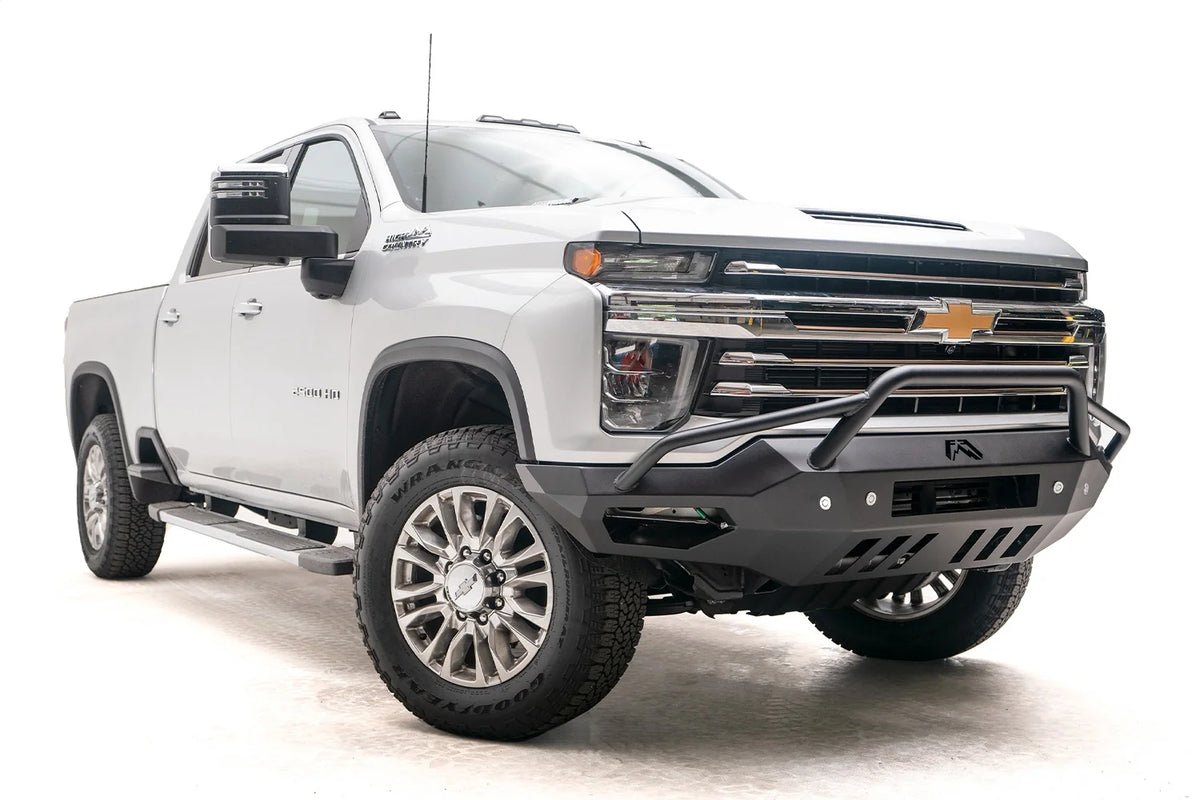 Fab Fours Vengeance front bumper with pre-runner guard on a white Chevrolet Silverado 2500HD, low front passenger-side three-quarter view, showing the tubular pre-runner hoop, angular end wings and slotted skid plate