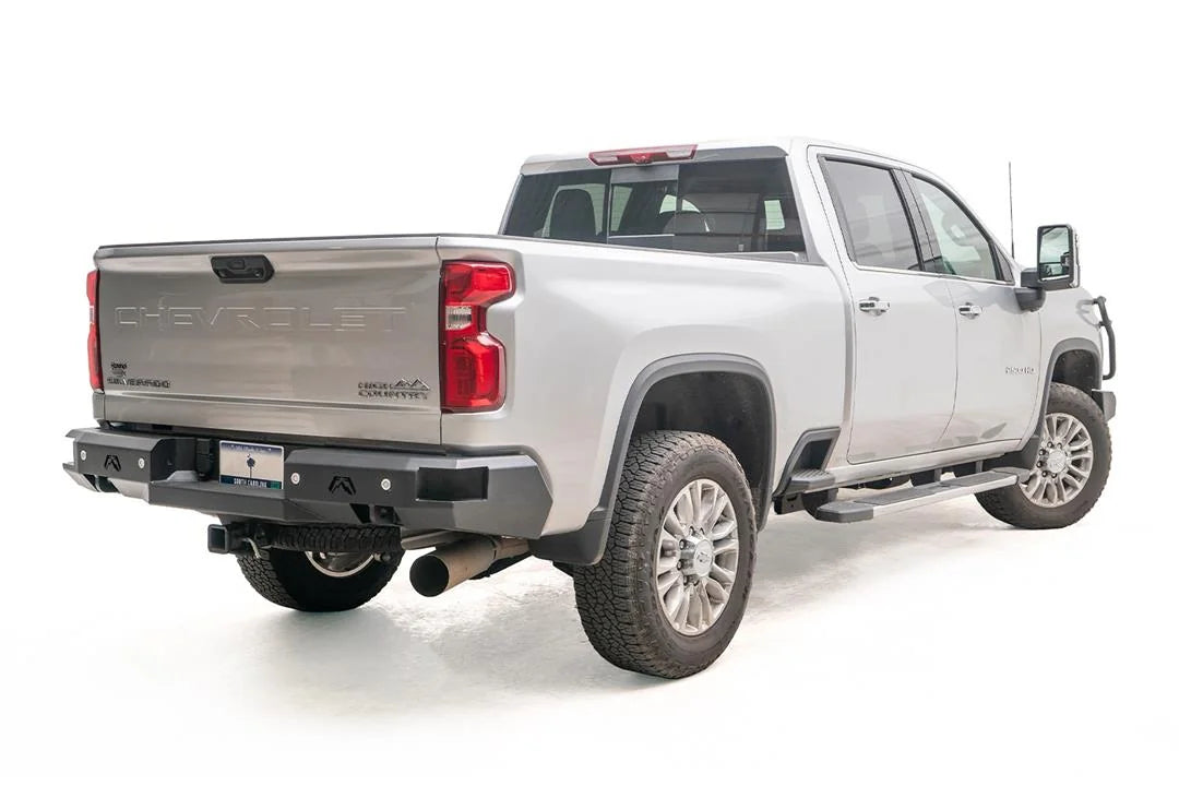 Fab Fours Premium rear bumper on a silver Chevrolet Silverado 2500HD, rear passenger-side three-quarter view, showing the black steel bumper, integrated rear lights and logo cutouts