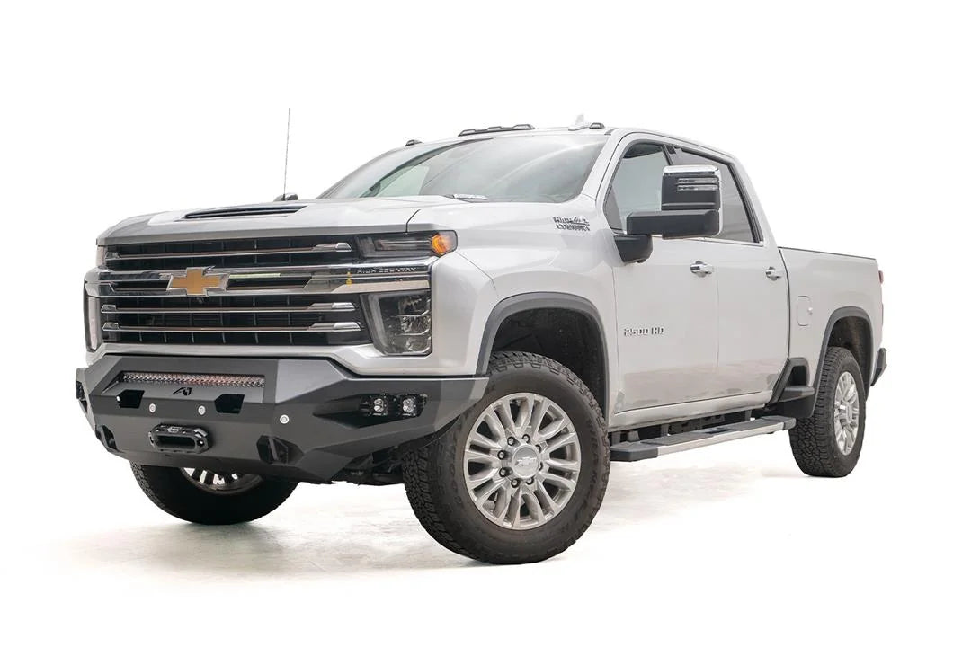 Fab Fours Matrix front bumper on a silver Chevrolet Silverado 2500HD, front driver-side three-quarter view, showing the no-guard design, integrated light bar and winch mount