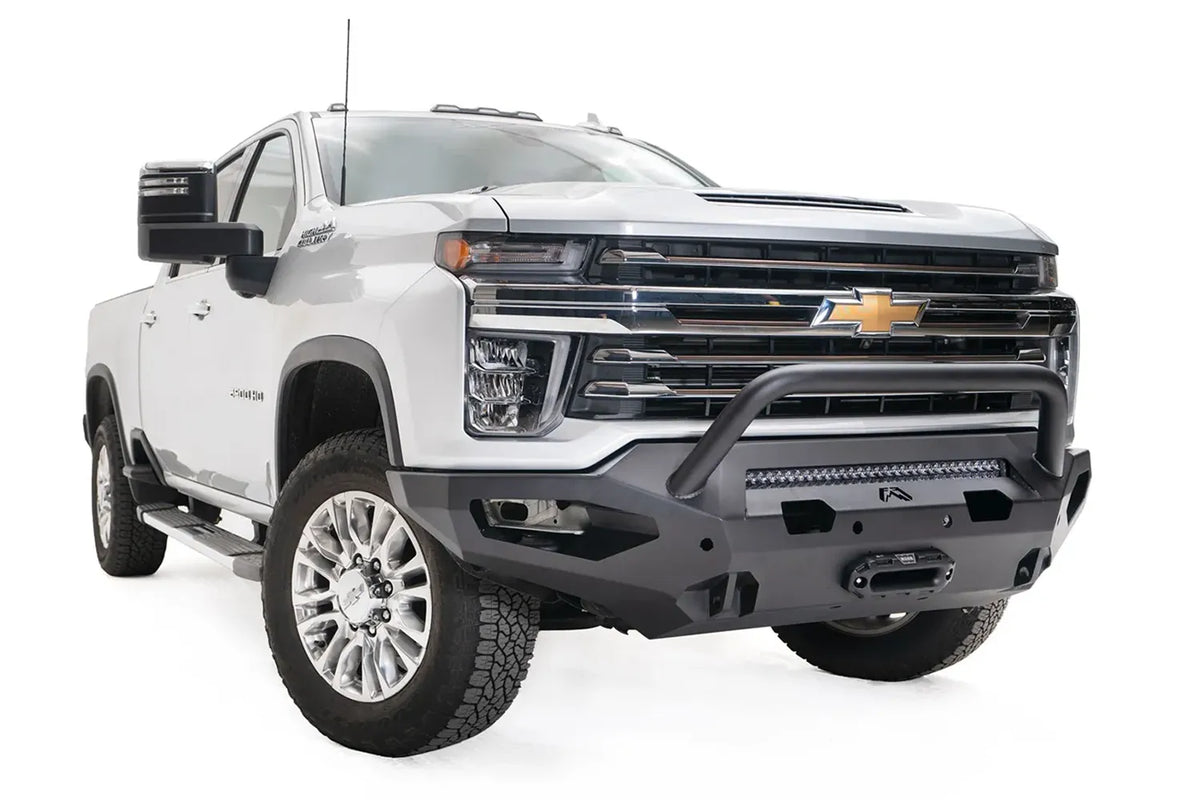 Fab Fours Matrix front bumper with pre-runner guard on a white Chevrolet Silverado 2500HD, front passenger-side three-quarter view, showing the tubular pre-runner hoop, integrated light bar and recessed winch mount