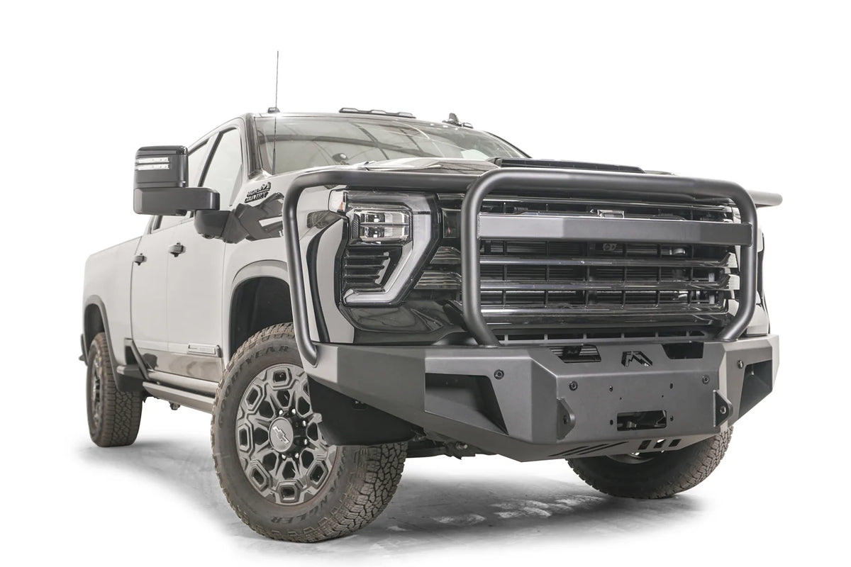 Fab Fours Premium Winch front bumper with full guard on a dark gray Chevrolet Silverado 2500HD, front passenger-side three-quarter view, showing the tubular full grille guard, winch mount and angled end wings