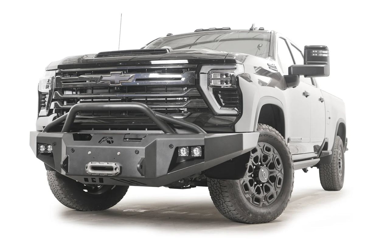 Fab Fours Premium Winch front bumper with pre-runner guard on a black Chevrolet Silverado 2500HD, front passenger-side three-quarter view, showing the tubular pre-runner hoop, winch fairlead and pod light cutouts