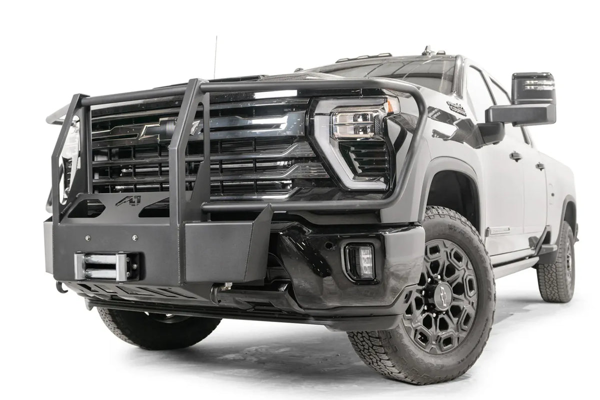 Fab Fours Winch Mount with full guard on a black Chevrolet Silverado 2500HD, front driver-side three-quarter view, showing the tubular full grille guard, boxed winch plate and roller fairlead