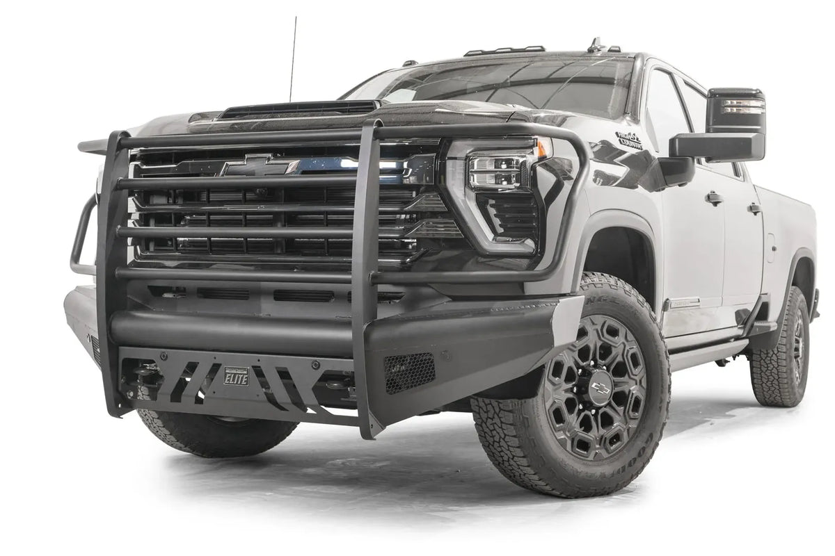 Fab Fours Black Steel Elite front bumper with full guard on a black Chevrolet Silverado 2500HD, front driver-side three-quarter view, showing the tubular full grille guard, slotted skid plate and mesh side vents
