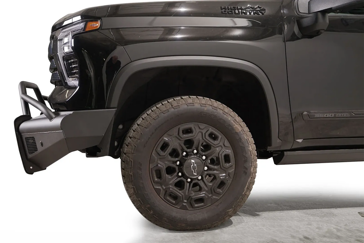 Fab Fours Black Steel Elite front bumper with pre-runner guard on a black Chevrolet Silverado 2500HD, side close-up of the front corner, showing the pre-runner tube, bumper end wing and wheel clearance