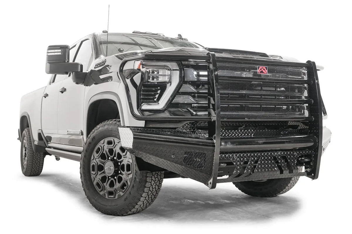 Fab Fours Black Steel front bumper with full guard on a black Chevrolet Silverado 2500HD, front passenger-side three-quarter view, showing the mesh-filled guard, diamond-plate end wing and slotted skid plate