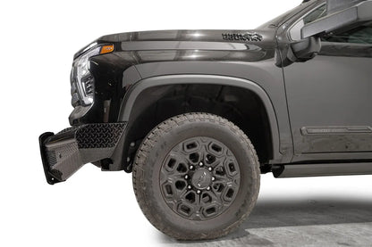 Fab Fours Black Steel front bumper on a black Chevrolet Silverado 2500HD, side close-up of the front corner, showing the diamond-plate end wing and wheel clearance