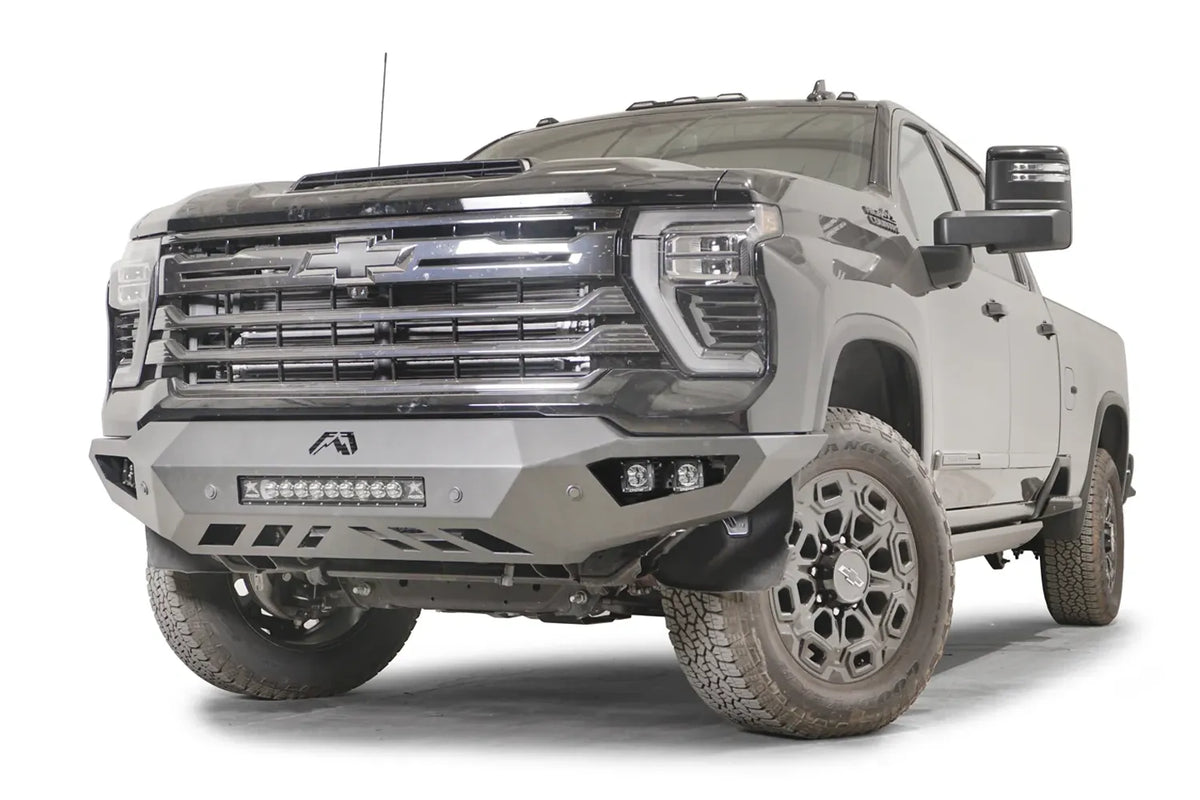 Fab Fours Vengeance front bumper on a dark gray Chevrolet Silverado 2500HD, front driver-side three-quarter view, showing the angular end wings, integrated light bar and slotted skid plate
