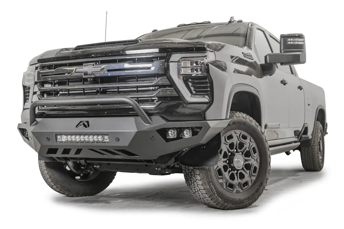 Fab Fours Vengeance front bumper with pre-runner guard on a dark gray Chevrolet Silverado 2500HD, front driver-side three-quarter view, showing the pre-runner hoop, integrated light bar and slotted skid plate