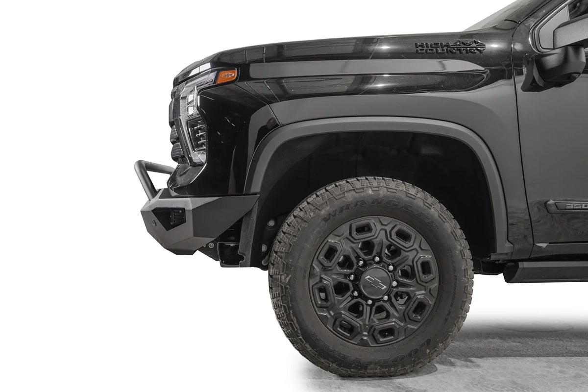 Fab Fours Vengeance front bumper with pre-runner guard on a black Chevrolet Silverado 2500HD, side close-up of the front corner, showing the pre-runner tube, angular end wing and wheel clearance