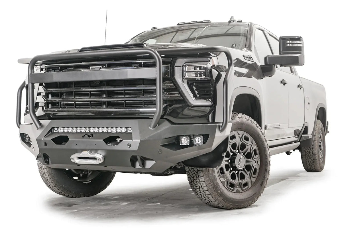 Fab Fours Matrix front bumper with full guard on a black Chevrolet Silverado 2500HD, front driver-side three-quarter view, showing the tubular guard, integrated light bar and pod light openings