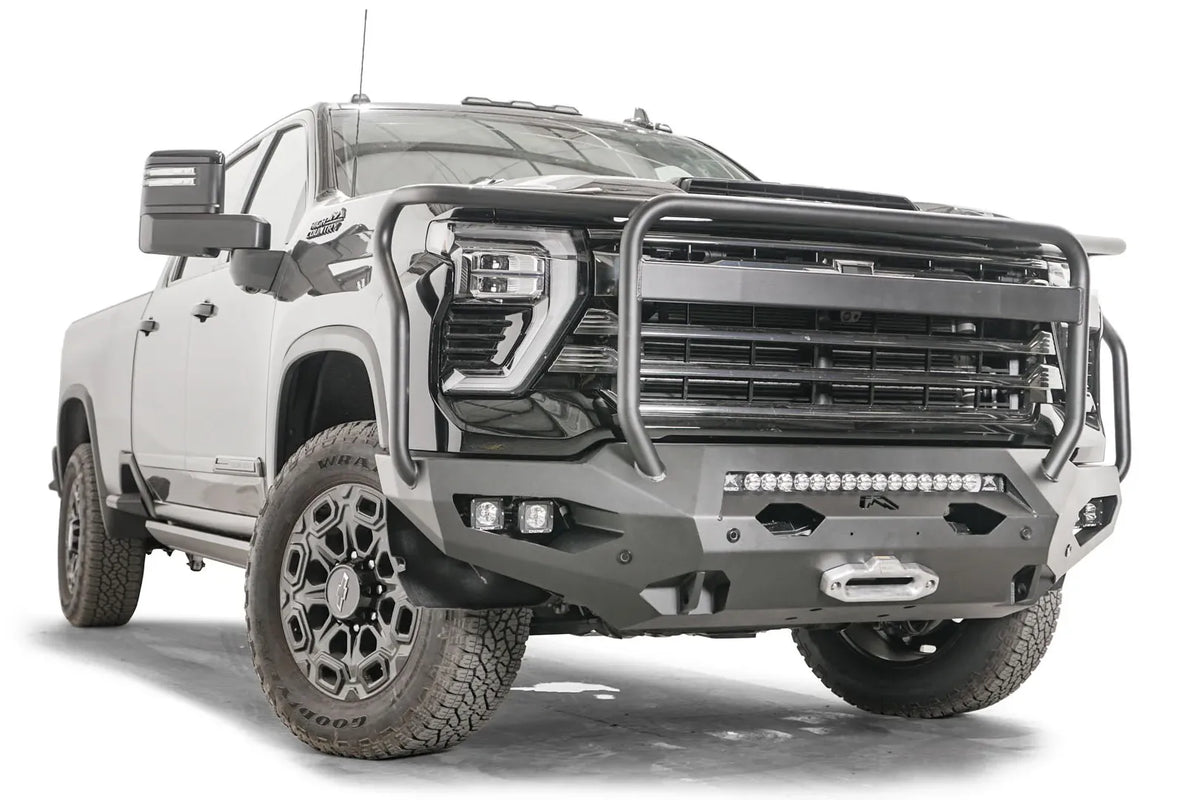 Fab Fours Matrix front bumper with full guard on a black Chevrolet Silverado 2500HD, front passenger-side three-quarter view, showing the tubular guard, integrated light bar and winch fairlead