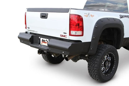 Fab Fours Black Steel Elite rear bumper on a white lifted GMC Sierra, rear passenger-side three-quarter view on a white background, showing the black steel face, wraparound end cap and center hitch receiver