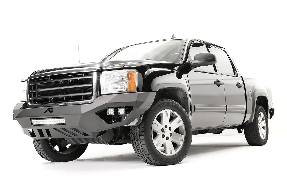 Fab Fours Vengeance front bumper on a black GMC Sierra 1500, front driver-side three-quarter view, showing the no-guard design, integrated light bar and cube light pods