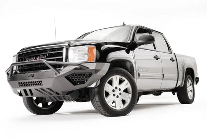 Fab Fours Vengeance front bumper with pre-runner guard on a black GMC Sierra 1500, front driver-side three-quarter view, showing the tubular pre-runner hoop, honeycomb mesh vents and slotted skid plate