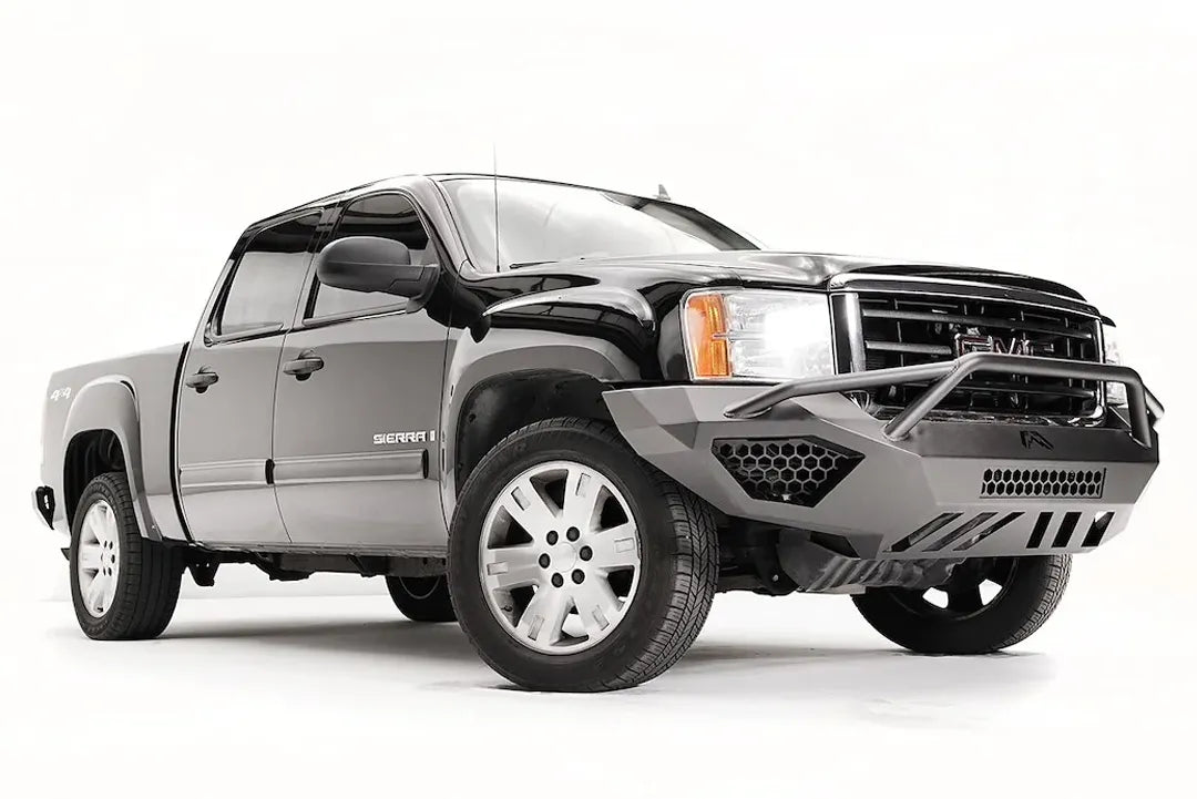 Fab Fours Vengeance front bumper with pre-runner guard on a black GMC Sierra 1500, front passenger-side three-quarter view, showing the pre-runner hoop, honeycomb mesh vent and angular end wing