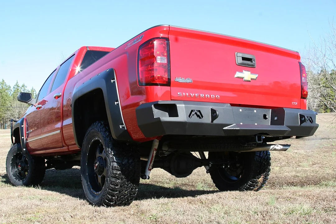 Fab Fours Premium rear bumper on a red lifted Chevrolet Silverado 1500, outdoor rear driver-side three-quarter view, showing the logo cutouts, D-ring mounts and wraparound end cap