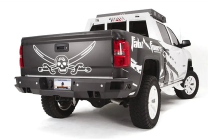 Fab Fours Premium rear bumper on a black and white wrapped lifted pickup, rear passenger-side three-quarter view, showing the black steel face, sensor cutouts and center hitch receiver