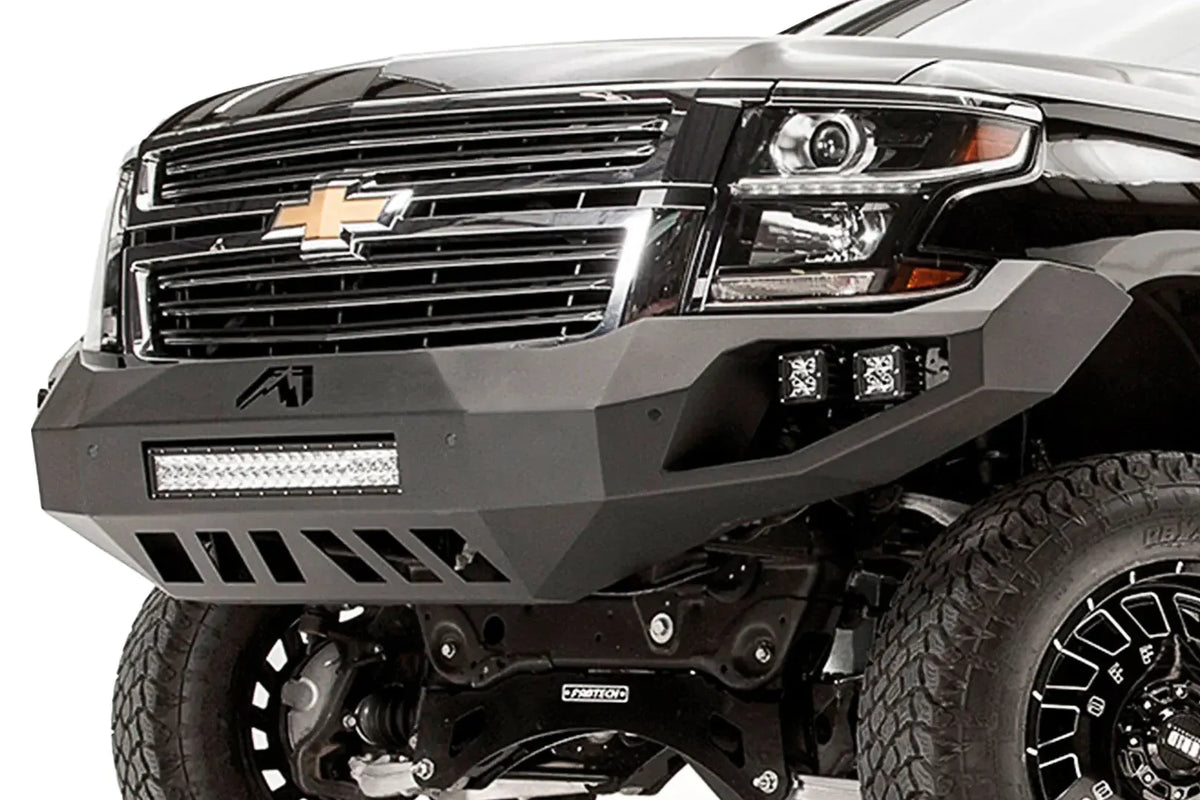 Fab Fours Vengeance front bumper on a black lifted Chevrolet Suburban, close-up of the front corner, showing the integrated light bar, cube light pods and slotted skid plate