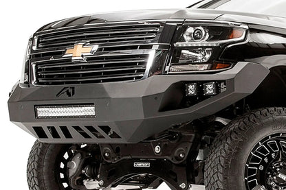 Fab Fours Vengeance front bumper on a black lifted Chevrolet Suburban, close-up of the front corner, showing the integrated light bar, cube light pods and slotted skid plate