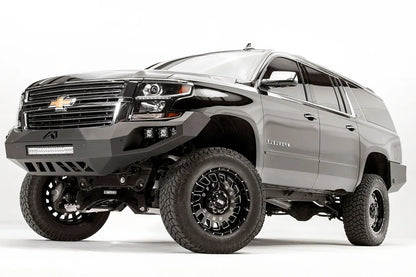Fab Fours Vengeance front bumper on a black lifted Chevrolet Suburban, front driver-side three-quarter view, showing the no-guard design, integrated light bar and cube light pods