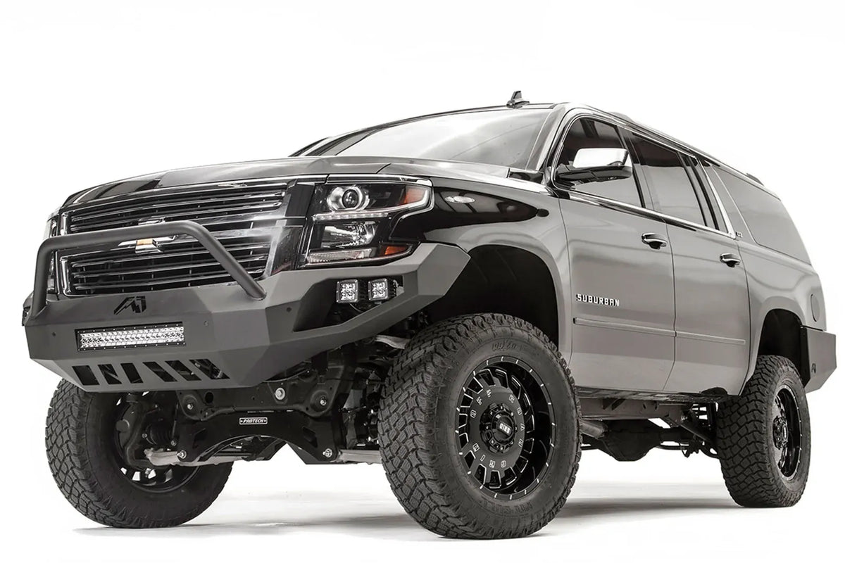 Fab Fours Vengeance front bumper with pre-runner guard on a black lifted Chevrolet Suburban, front driver-side three-quarter view, showing the pre-runner hoop, integrated light bar and slotted skid plate