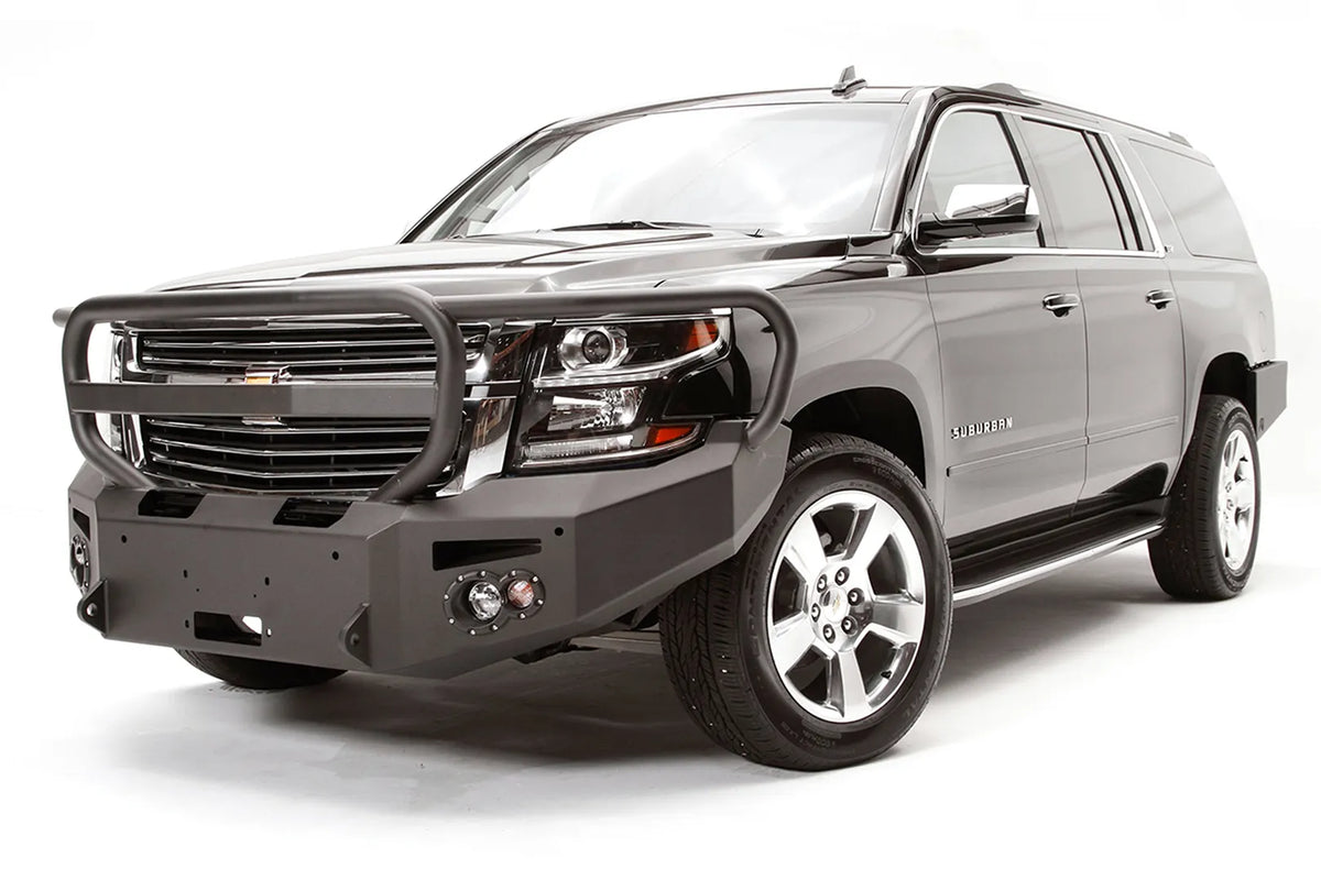 Fab Fours Premium Winch front bumper with full guard on a black Chevrolet Suburban, front driver-side three-quarter view, showing the tubular full grille guard, winch mount and round light cutouts