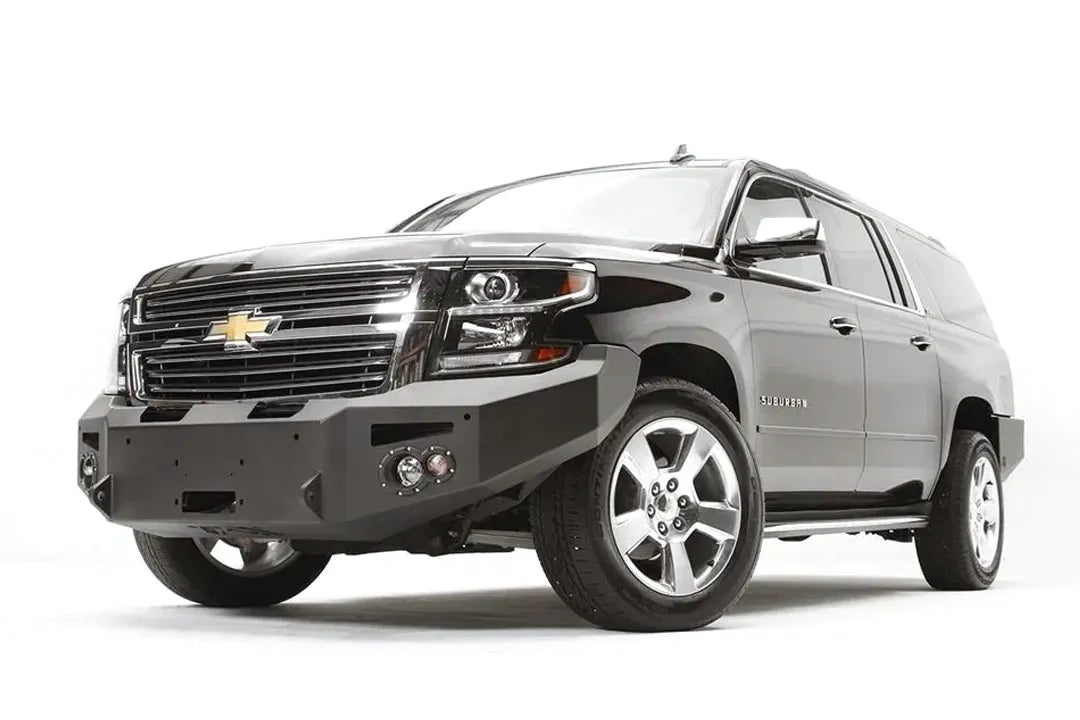 Fab Fours Premium Winch front bumper on a black Chevrolet Suburban, front driver-side three-quarter view, showing the no-guard design, winch mount and round light cutouts