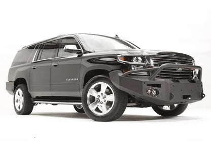 Fab Fours Premium Winch front bumper with pre-runner guard on a black Chevrolet Suburban, front passenger-side three-quarter view, showing the tubular pre-runner hoop, winch mount and round light cutouts