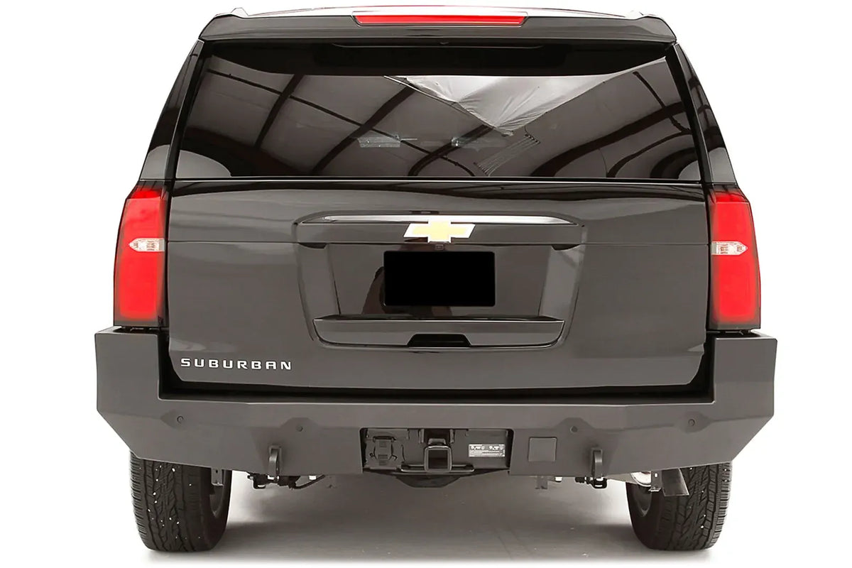 Fab Fours Premium rear bumper on a black Chevrolet Suburban, straight rear view, with parking sensors, center hitch receiver, and D-ring mounts